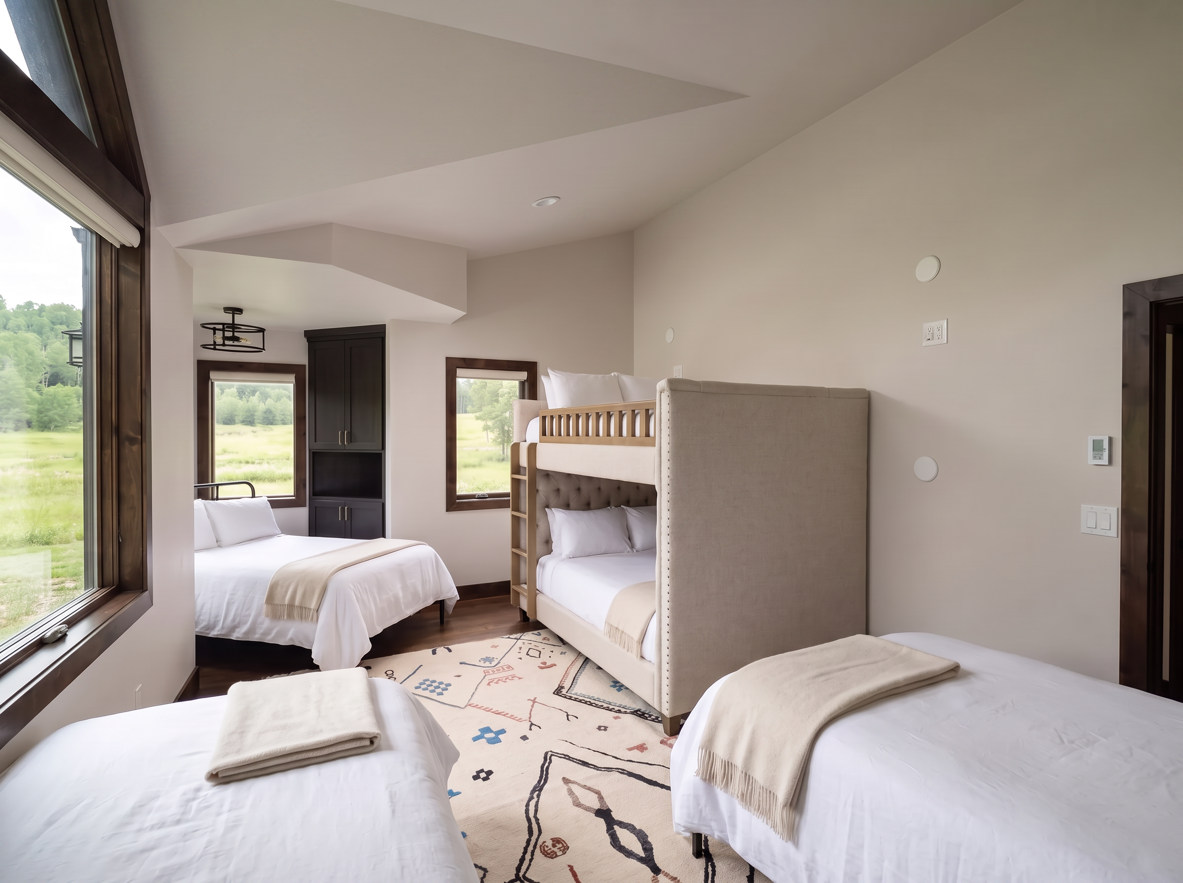 The bunk room with an upholstered bunk bed, twin beds in white linen, and a wool rug