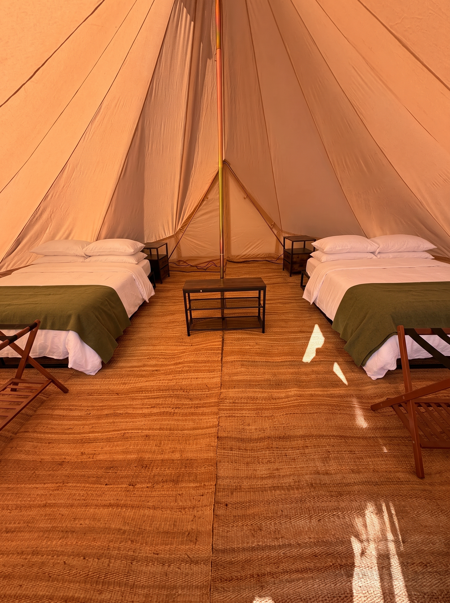 Inside a bell tent: two beds in white linen and olive wool on a jute rug